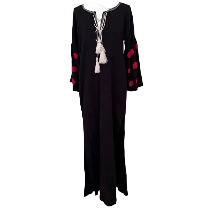 A black long-sleeve maxi dress with red floral embroidery on the sleeves and a white tassel necklace with lace-up front details, displayed on a white mannequin torso against a light gray background.