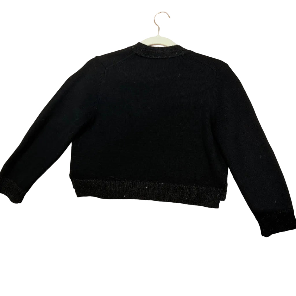 A black long-sleeve cropped sweater with textured knit cuffs and hem, laid flat on a peach-colored ribbed blanket.