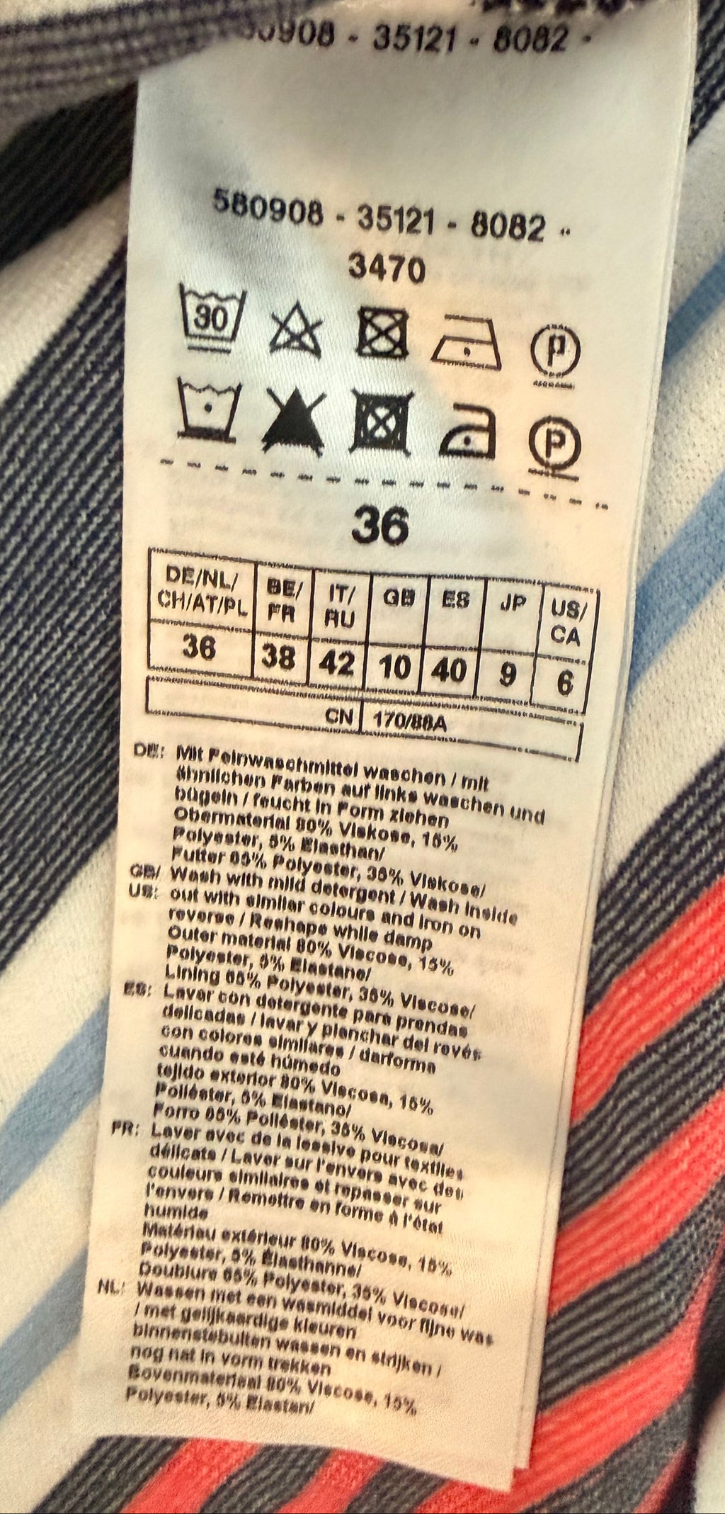 A close-up of a sewn-on garment care label attached to striped fabric with navy, white, red, and blue lines.