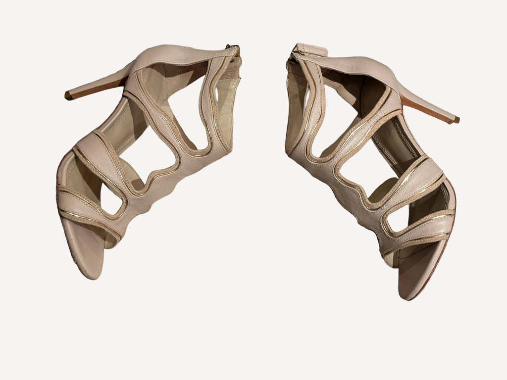 Bailey Grace Closet Concierge nude stiletto sandals with wavy cut-out straps and metallic piping on a wooden floor.