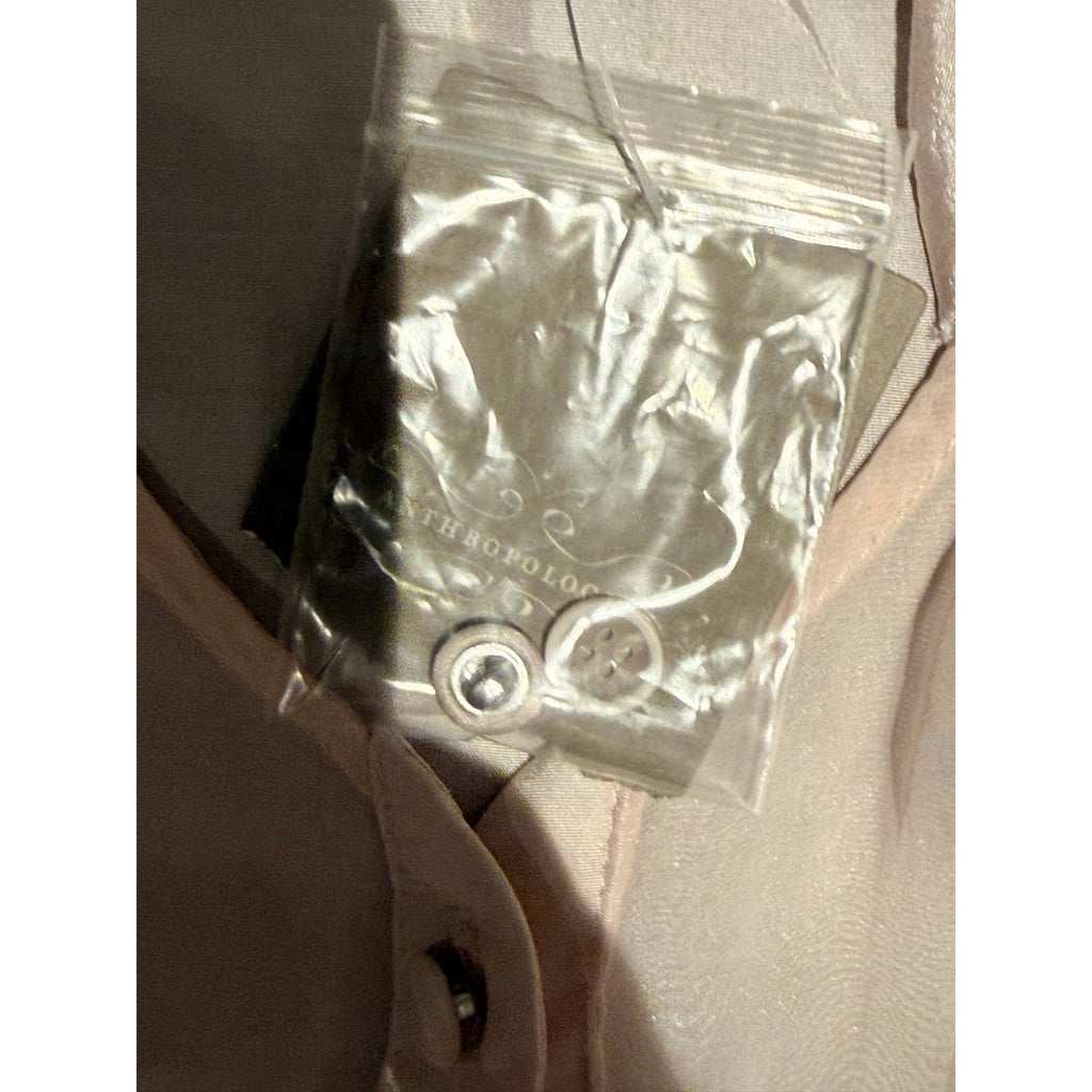 A small clear plastic bag containing two white buttons, placed on a light beige fabric surface.